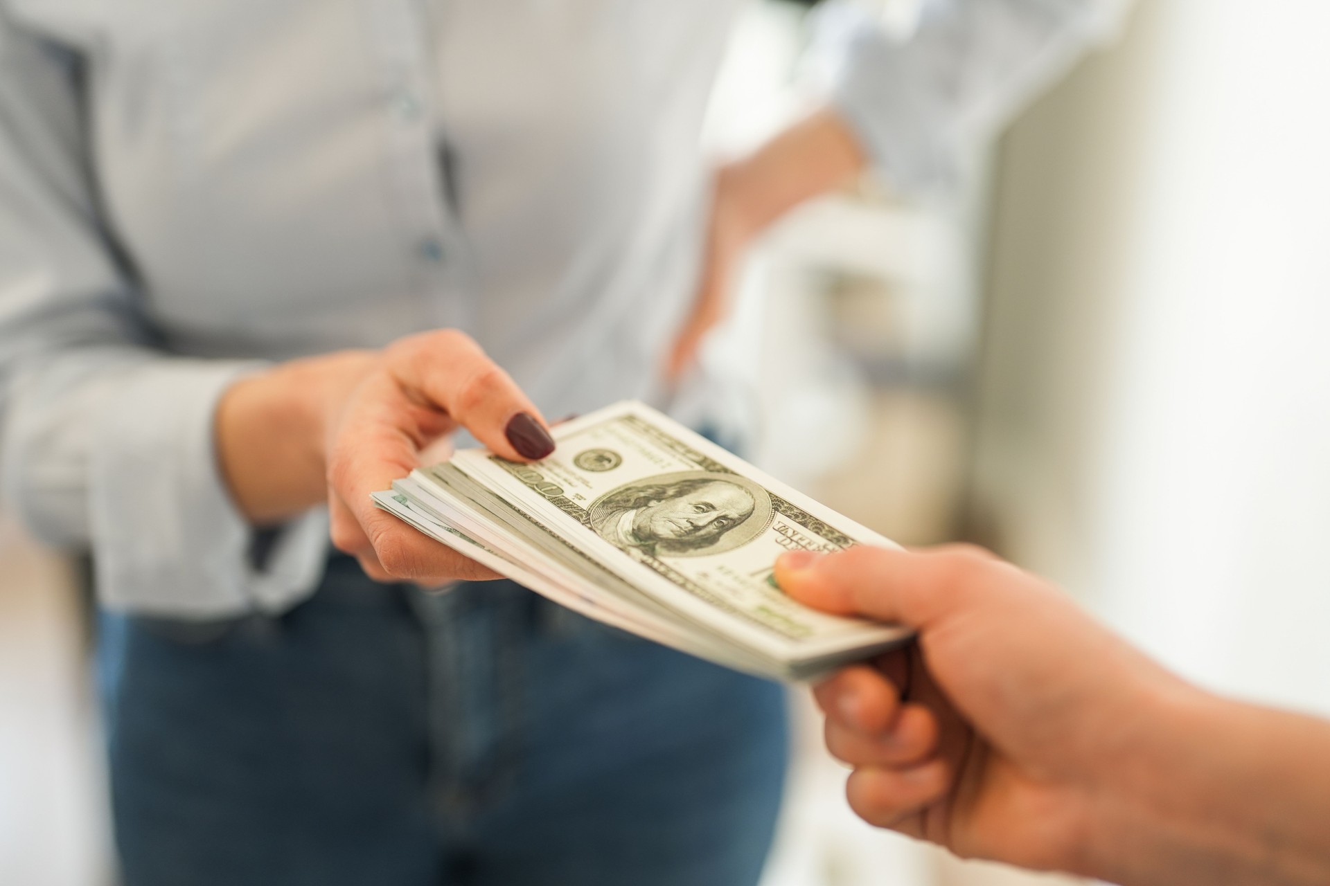 Close-up of woman handing stack of dollars to other person